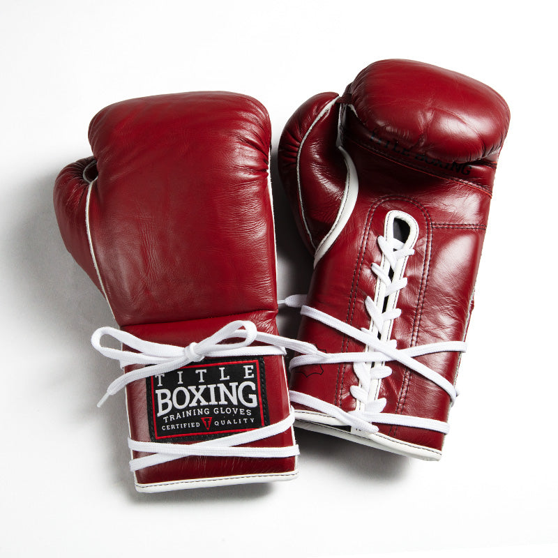 A pair of red leather boxing gloves with white laces, one glove showing a 'Title Boxing' brand patch on the wrist strap, set against a plain white background.