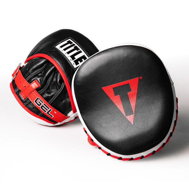 A pair of black leather boxing focus mitts with red and white trim, featuring the red and black Triangle logo on the front pad and the white TITLE brand name on the side.