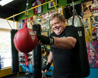 variant:black::TITLE Boxing Fight Back Semi-Elastic Hand Wraps guy hitting double end bag