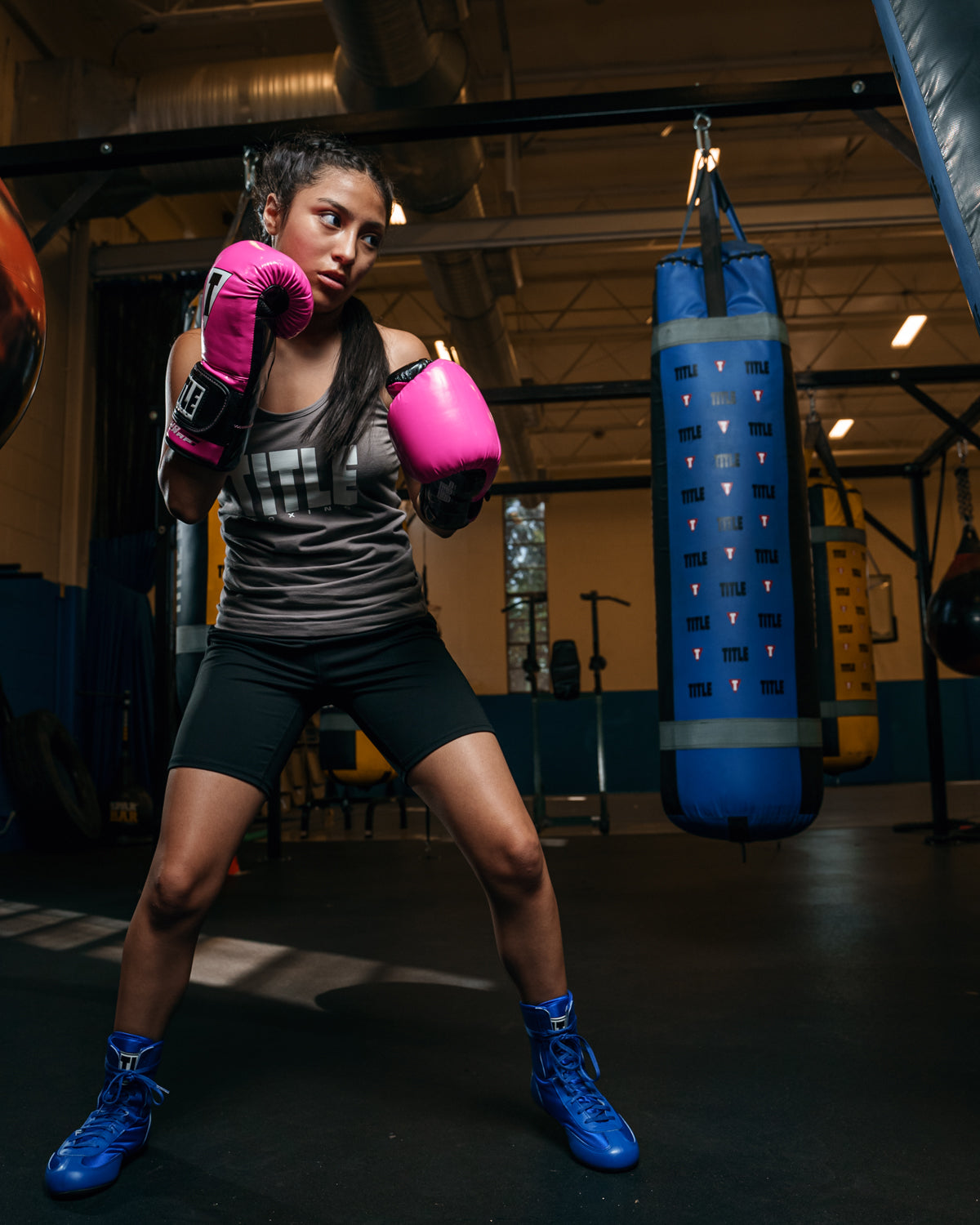 variant:Hot Pink/Black::TITLE Boxing Gel Glory Super Bag Gloves 2.0 girl boxing pose with bag