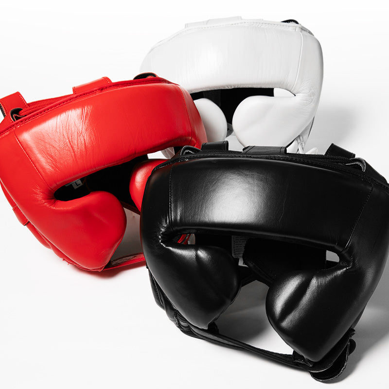 Three padded boxing headgear pieces in red, white, and black arranged together on a clean light gray studio background.