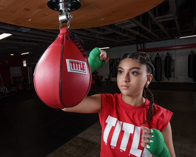 variant:green::TITLE Boxing Select 180" Semi Elastic Mexican Hand Wraps girl hitting a speed bag